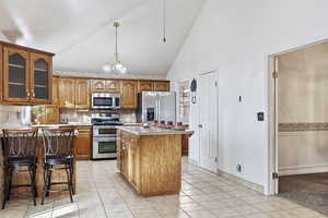 Kitchen with light tile patterned floors, backsplash, hanging light fixtures, stainless steel appliances, and a center island