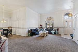 Living room with ornamental molding, carpet floors, and an inviting chandelier