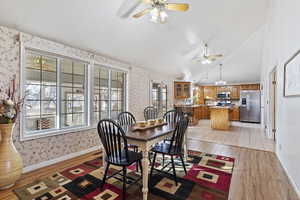 Dining room featuring vaulted ceiling, ceiling fan with notable chandelier, and light hardwood / wood-style floors