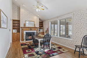 Dining space with a tiled fireplace, wood-type flooring, vaulted ceiling, and ceiling fan