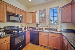 Kitchen with black appliances, dark stone counters, light hardwood / wood-style flooring, and sink