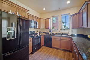 Kitchen featuring sink, hardwood / wood-style floors, black appliances, and dark stone countertops