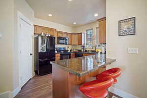 Kitchen with dark wood-type flooring, black appliances, kitchen peninsula, and a breakfast bar area