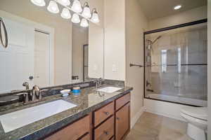 Full bathroom with shower / bath combination with glass door, vanity, toilet, and tile patterned flooring