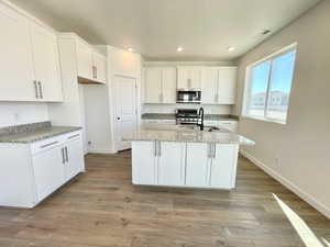 Kitchen featuring an island with sink, sink, white cabinets, light stone counters, and stainless steel appliances