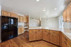 Kitchen with dark wood-type flooring, built in desk, black fridge with ice dispenser, decorative light fixtures, and kitchen peninsula