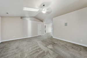 Additional living space with vaulted ceiling with skylight and light colored carpet