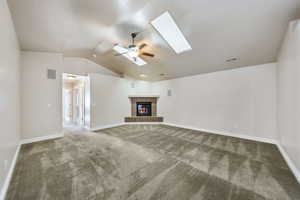 Unfurnished living room with ceiling fan, carpet, vaulted ceiling with skylight, and a fireplace