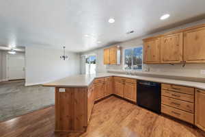 Kitchen featuring sink, black dishwasher, kitchen peninsula, pendant lighting, and light hardwood / wood-style floors