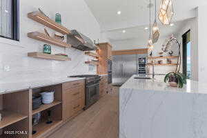 Kitchen with range hood, decorative light fixtures, sink, backsplash, and electric stove