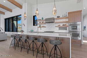 Kitchen featuring double oven, pendant lighting, a kitchen bar, and range hood