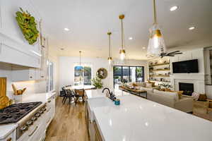 Kitchen with white cabinetry, a fireplace, decorative light fixtures, stainless steel gas stovetop, and light wood-type flooring