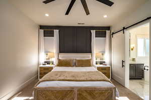 Bedroom featuring a barn door, ceiling fan, and ensuite bathroom