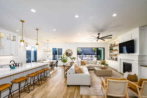 Living room with light hardwood / wood-style flooring, a brick fireplace, built in shelves, and plenty of natural light