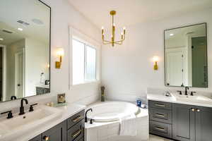 Bathroom with vanity, a chandelier, and tiled tub