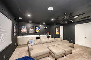 Carpeted home theater room featuring bar and ceiling fan