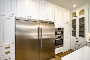 Kitchen with stainless steel appliances, white cabinetry, light wood-type flooring, and light stone counters