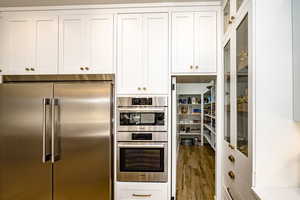 Kitchen with appliances with stainless steel finishes, hardwood / wood-style floors, and white cabinets