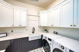 Clothes washing area with sink, washer and clothes dryer, and cabinets