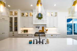 Kitchen featuring stainless steel gas stovetop, light stone countertops, white cabinets, and backsplash