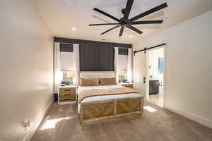 Carpeted bedroom with a barn door and ceiling fan