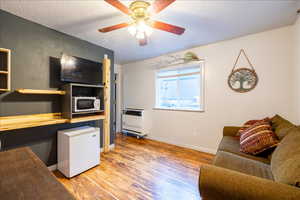 Living room featuring a textured ceiling, heating unit, light hardwood / wood-style flooring, and ceiling fan