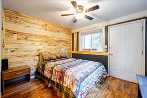 Bedroom featuring a textured ceiling, ceiling fan, dark wood-type flooring, and wooden walls