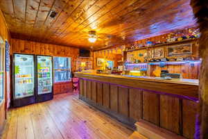 Bar featuring wooden walls, ceiling fan, wood ceiling, and light hardwood / wood-style floors