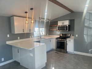 Kitchen featuring white cabinets, stainless steel appliances, sink, hanging light fixtures, and lofted ceiling with beams