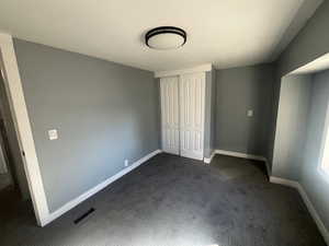 Unfurnished bedroom featuring dark carpet and a closet