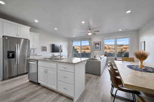 Kitchen featuring appliances with stainless steel finishes, white cabinetry, an island with sink, light stone countertops, and a textured ceiling