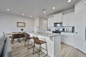 Kitchen with white cabinetry, a kitchen island with sink, a kitchen breakfast bar, stainless steel appliances, and light hardwood / wood-style floors