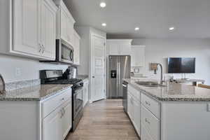 Kitchen with sink, white cabinets, stainless steel appliances, light stone countertops, and light wood-type flooring