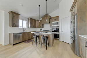 Kitchen with stainless steel appliances, decorative light fixtures, a breakfast bar, a center island, and sink