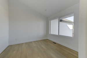 Spare room featuring light wood-type flooring and vaulted ceiling