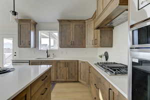 Kitchen featuring light hardwood / wood-style flooring, sink, decorative light fixtures, white dishwasher, and stainless steel gas cooktop