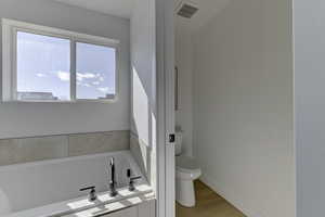 Bathroom featuring hardwood / wood-style flooring, tiled bath, toilet, and a healthy amount of sunlight