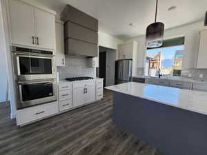 Kitchen with tasteful backsplash, black appliances, pendant lighting, light stone countertops, and dark wood-type flooring