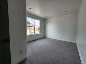 Empty room with visible vents, dark carpet, a textured ceiling, and baseboards