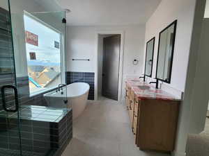 Full bath with a shower with shower door, a freestanding tub, a sink, tile walls, and double vanity