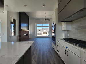Kitchen featuring dark wood-style flooring, a brick fireplace, exhaust hood, ceiling fan, and appliances with stainless steel finishes