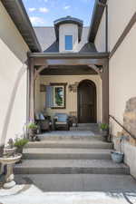 View of exterior entry featuring stucco siding and a shingled roof