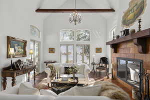 Living room with a tiled fireplace, an inviting chandelier, beamed ceiling, and high vaulted ceiling