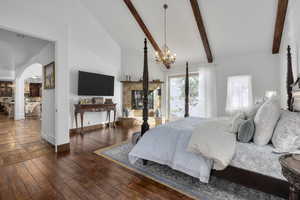 Bedroom featuring a notable chandelier, a tiled fireplace, dark wood-type flooring, and lofted ceiling with beams