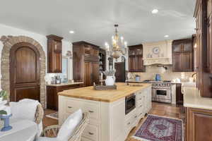 Kitchen with hanging light fixtures, a kitchen island with sink, decorative backsplash, butcher block counters, and built in appliances