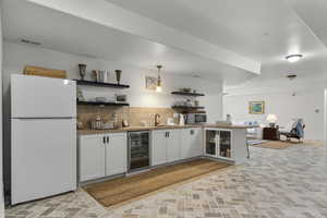 Bar featuring decorative backsplash, white cabinets, decorative light fixtures, white refrigerator, and beverage cooler