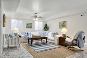 Living room featuring ceiling fan, a wealth of natural light, and a raised ceiling