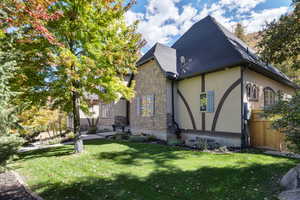 View of property exterior with a lawn, stucco siding, stone siding, and a shingled roof
