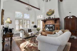 Living room with dark wood-type flooring, beamed ceiling, a notable chandelier, high vaulted ceiling, and a tiled fireplace