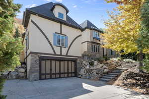 View of front facade featuring stone siding, stairway, stucco siding, and concrete driveway